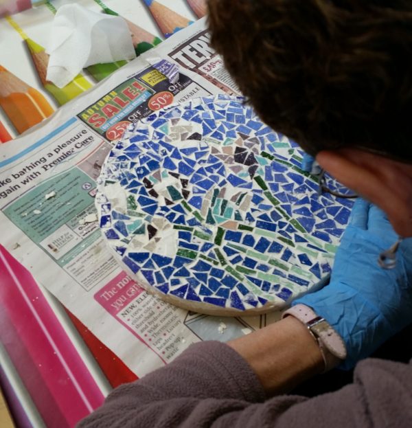 a man carefully crafting mosaic out of broken blue tiles