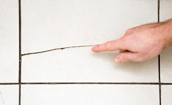 a hand pointing at a crack on the tiles