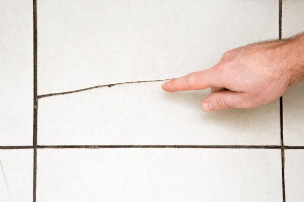 A hand pointing at the crack on the tile